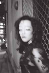 a black and white photo of a woman leaning against a fence