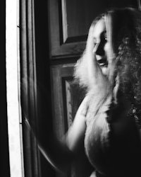 a black and white photo of a woman looking out a window