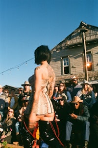 a woman in a leather dress is riding a skateboard in front of a crowd